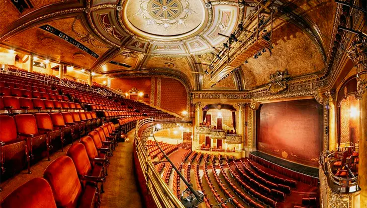 Intérieur de théâtre orné, avec sièges rouges et plafond décoratif.