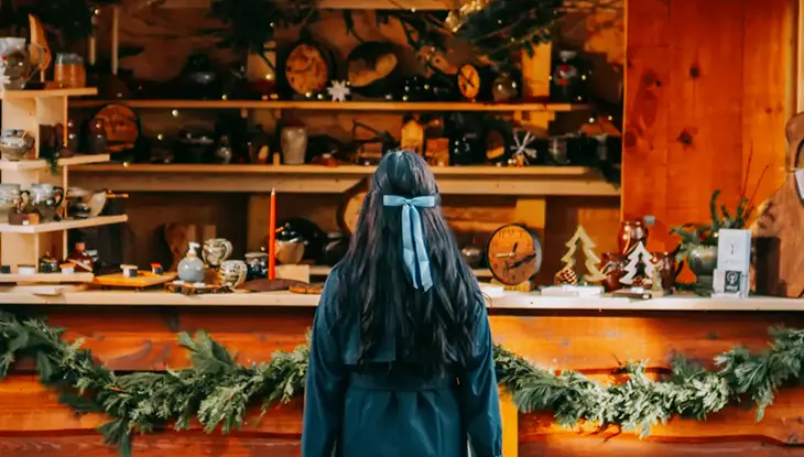 Visitor browsing a rustic Christmas market stall filled with seasonal decorations and gifts.