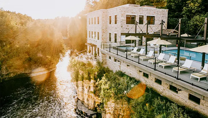 L’hôtel et spa Elora Mill surplombant la rivière Grand, avec des chaises longues au bord de la piscine au coucher du soleil.