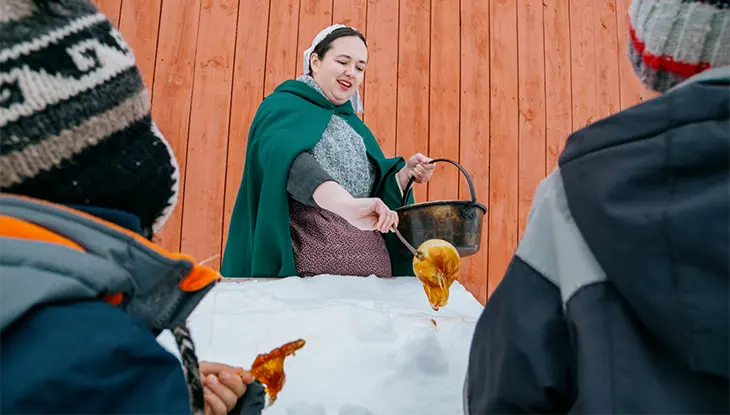 Person pouring hot maple syrup onto snow for visitors to enjoy during the Essex Maple Syrup Festival.