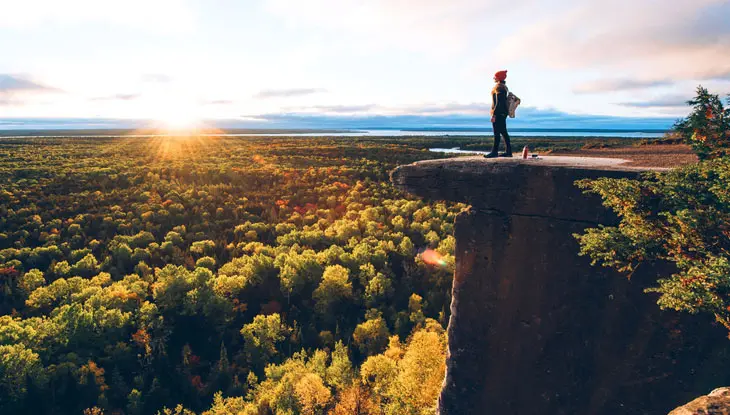 Une femme se tient au sommet d'une falaise, admirant le feuillage d'automne pittoresque en contrebas.