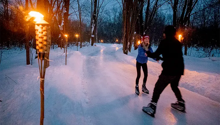 Una pareja patinando sobre hielo en la pista de patinaje en Fern Resort iluminada por la noche con antorchas tiki.