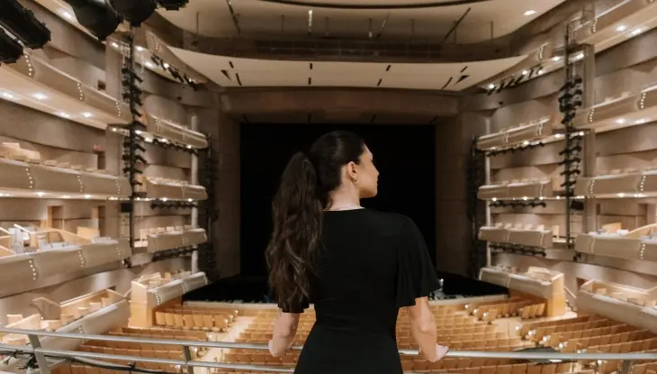 Una mujer está de pie en un balcón con vistas a un salón vacío en el Centro de Artes Escénicas Four Seasons.