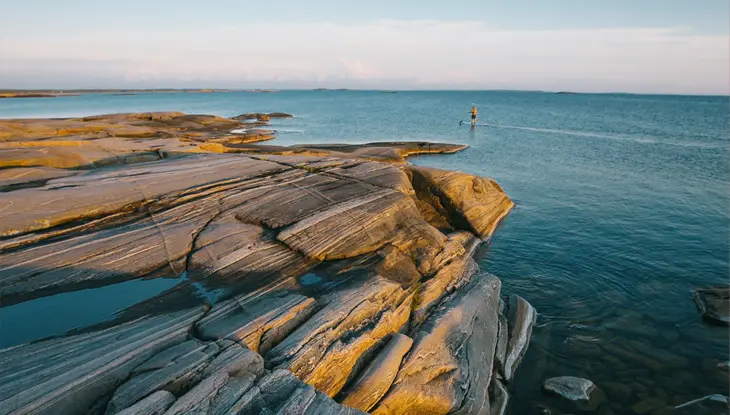 A person paddles past a rocky outcropping on a calm day on Georgian Bay.