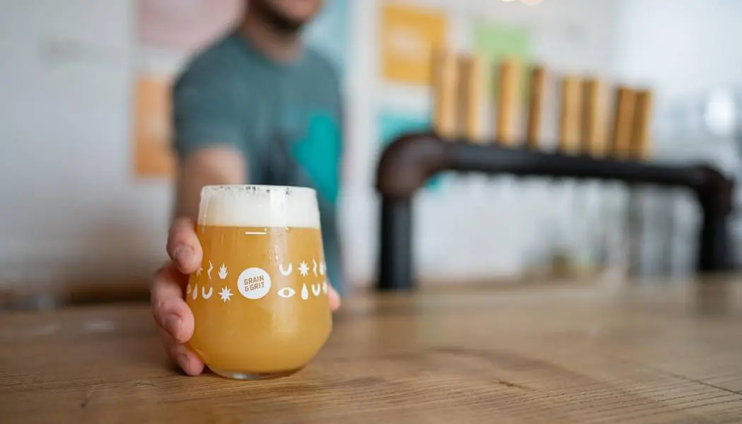 Close-up of a person serving a freshly poured craft beer on the wooden bar of a craft brewery in Hamilton.
