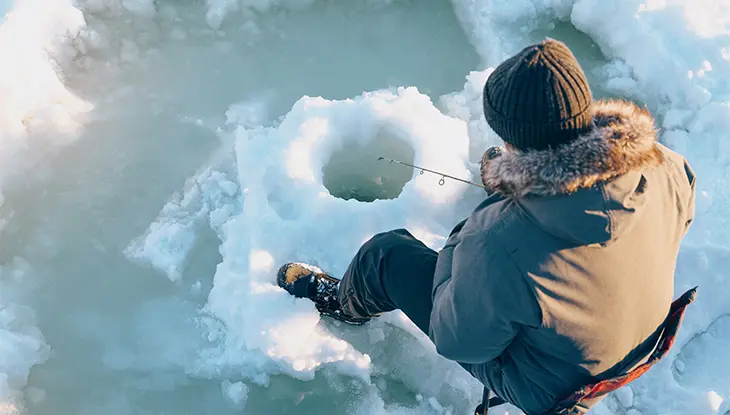 Una persona pesca en el hielo junto a un agujero en el lago congelado.