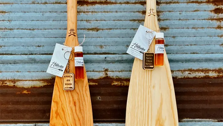 Zwei handgefertigte Kanupaddel aus Holz, die vor einer Wellblechwand ausgestellt sind.