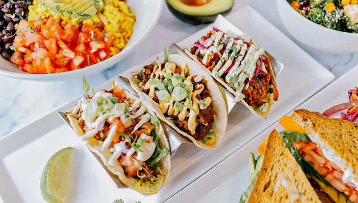 Vegan tacos served with bowls of avocado, beans and fresh vegetables on a bright table.