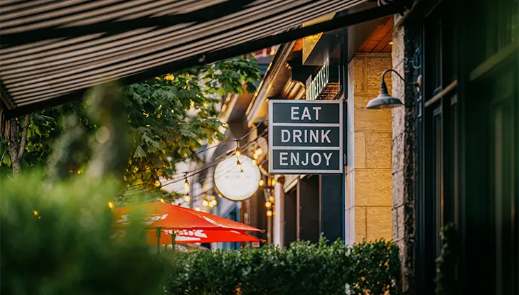 Restaurantfassade mit dem Schild „Eat Drink Enjoy“ und Sitzgelegenheiten auf der Terrasse in Hamilton, Ontario.
