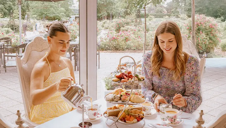 Two women enjoying afternoon tea at a garden terrace table.