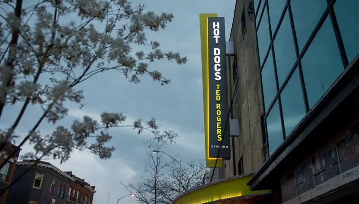 A long rectangular green and black sign that reads “HOT DOCS” protrudes from the side of a building.