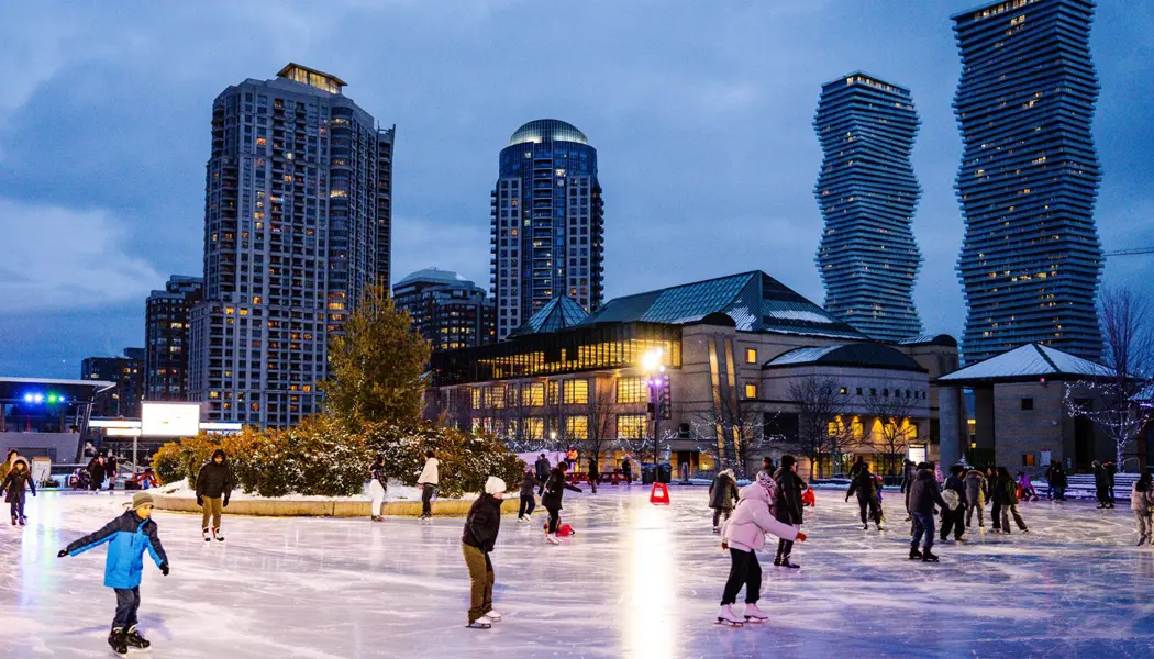 A group of people ice skating at dusk on a well-lit rink at Celebration Square in Mississauga.