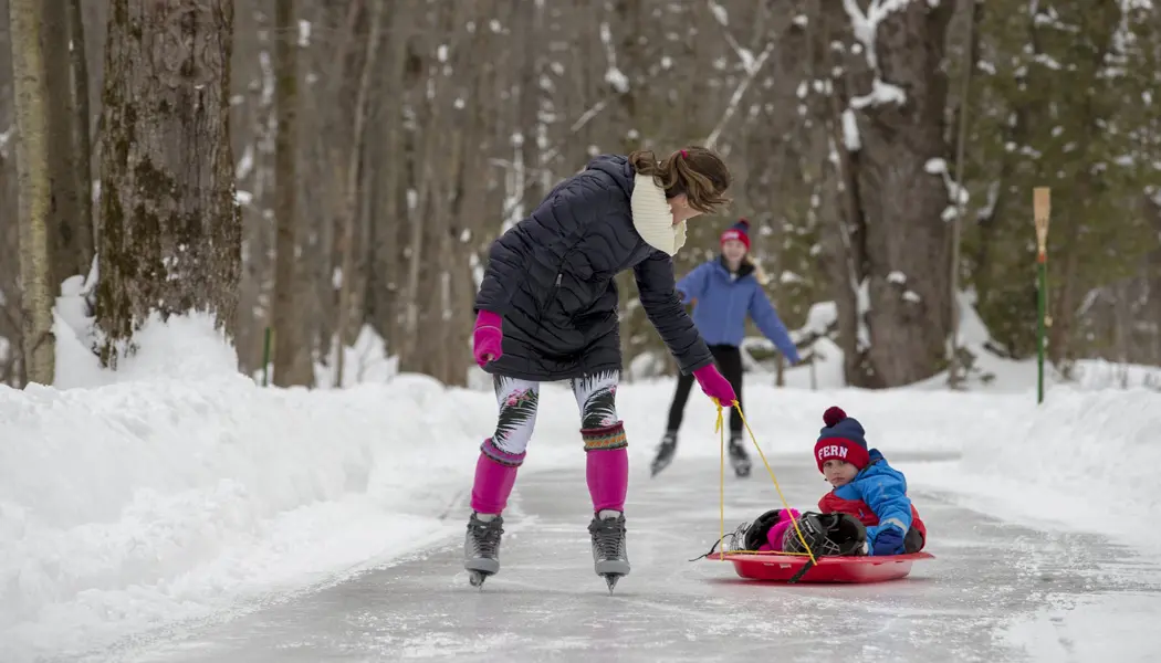 Une femme qui fait du patin à glace tire un jeune enfant sur une luge derrière elle.