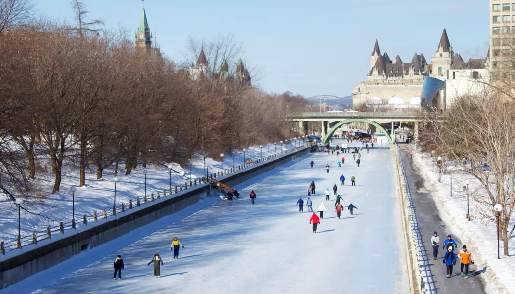 Crowds of people ice skating along the famous Rideau Canal Skateway with historic Ottawa architecture in the background.