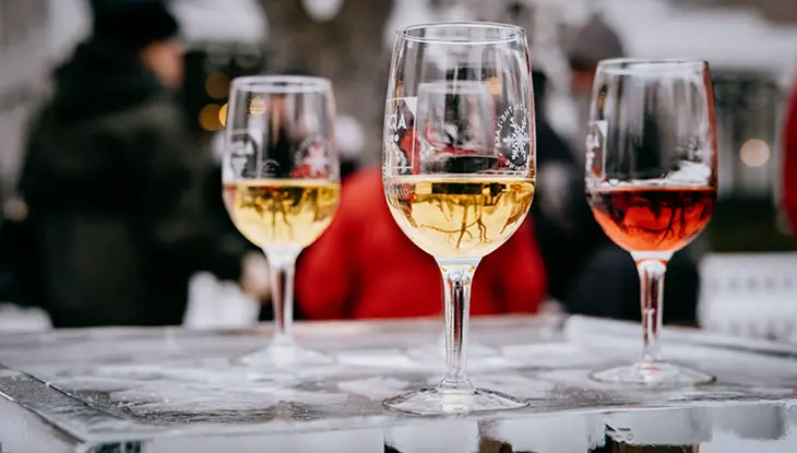 Three wine glasses with ice wine sit on a table in front of a group of people.