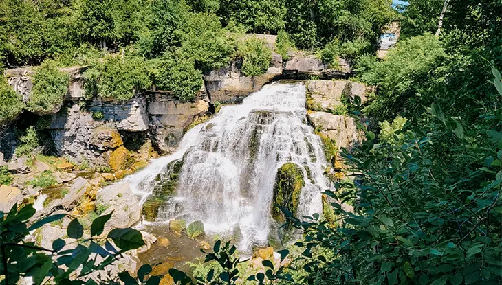 Chute d’eau se déversant sur des falaises rocheuses, entourée de forêt.