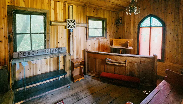 Interior of a small wooden chapel with simple pews, altar and natural light coming through the windows.