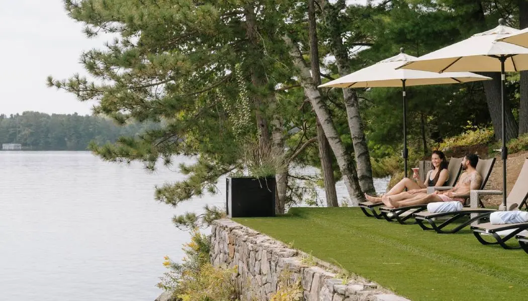 Un couple se détend sur des chaises longues extérieures surplombant les eaux calmes du lac Rosseau dans un centre de bien-être à Muskoka.