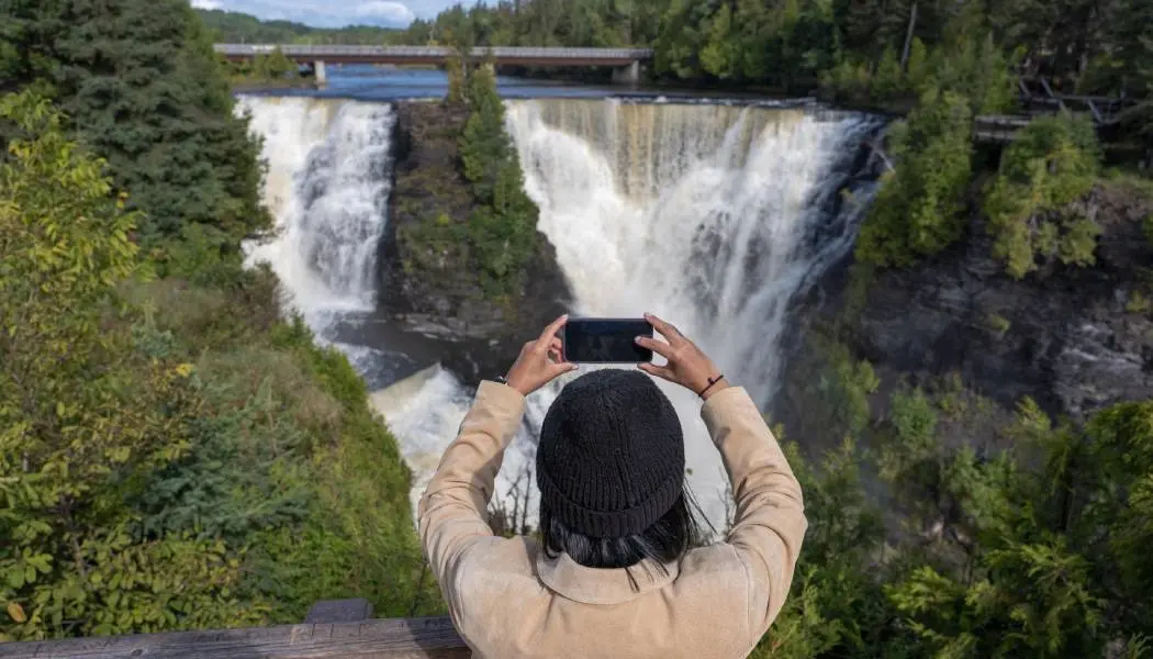 A woman takes a photo on her phone of the double cascade at Kakabeka Falls near Thunder Bay.