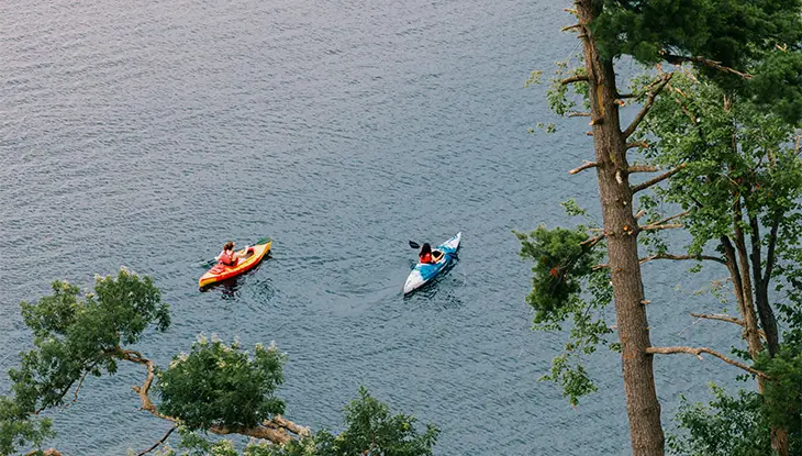 Dos personas practicando kayak en un lago, vistas desde arriba a través de los árboles.