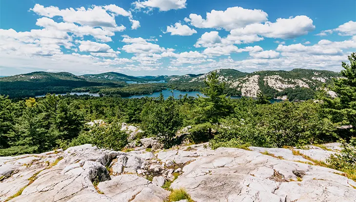 Vue panoramique des crêtes granitiques et des lacs bleus du parc provincial Killarney, sous un ciel parsemé de nuages blancs.