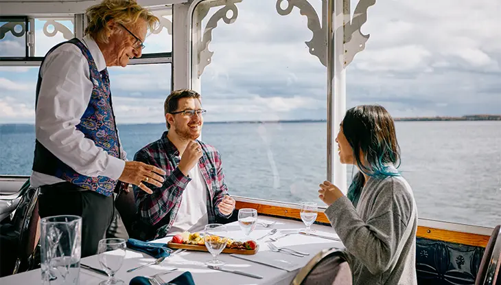 Una pareja disfruta de un brunch en un barco con grandes ventanales con vistas al agua.
