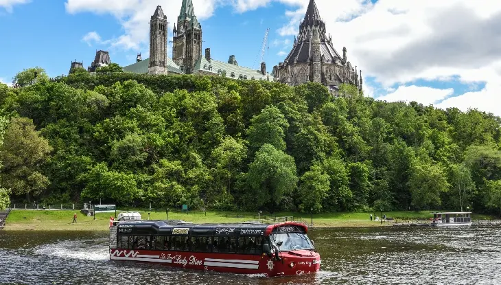 Un bateau de tourisme flottant sur l'eau avec les bâtiments du Parlement d'Ottawa en arrière-plan..