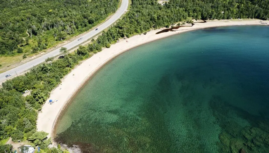 A white, sandy beach shoreline extends alongside the blue waters of Lake Superior.