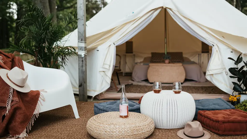 Two wine glasses are positioned on ottomans outside a white glamping tent.