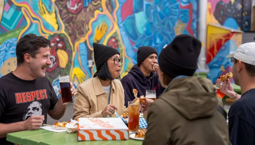 Un grupo de amigos disfruta de pizza recién hecha y cerveza en una mesa de una terraza en Thunder Bay.