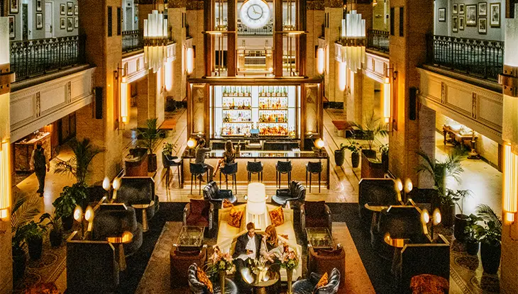 Large historic hotel lobby with chandeliers, seating areas and guests gathered around a central space.