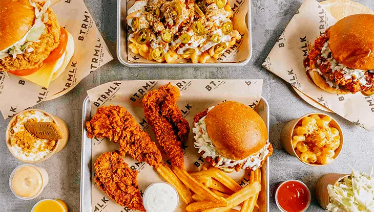 Sándwiches de pollo frito, papas fritas y guarniciones servidos en una mesa de restaurante.