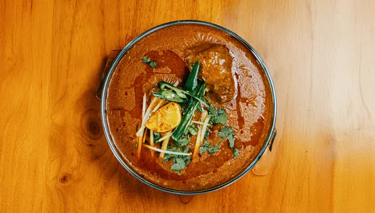 Un bol de curry indio aderezado con hierbas frescas y jengibre sobre una mesa de madera.