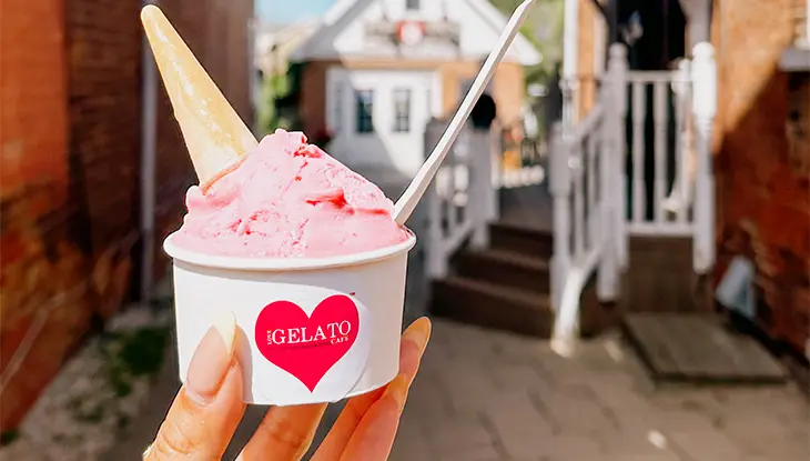 : Personne tenant une coupe de gelato à la fraise, avec un cornet et une cuillère, à l’extérieur.