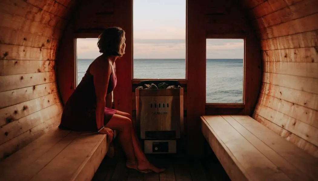 Femme qui se détend à l’intérieur d’un sauna dans un tonneau de cèdre au bord des eaux calmes du lac Érié.