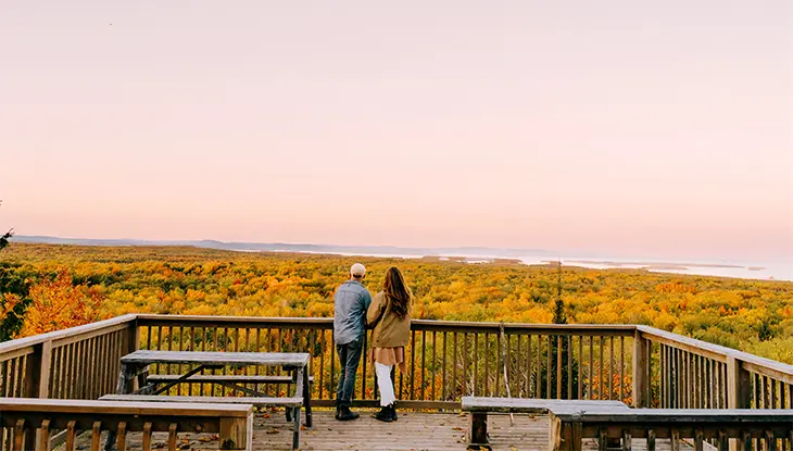 Couple standing at a wooden lookout overlooking vibrant fall colours on the Bebamikawe Trail on Manitoulin Island.
