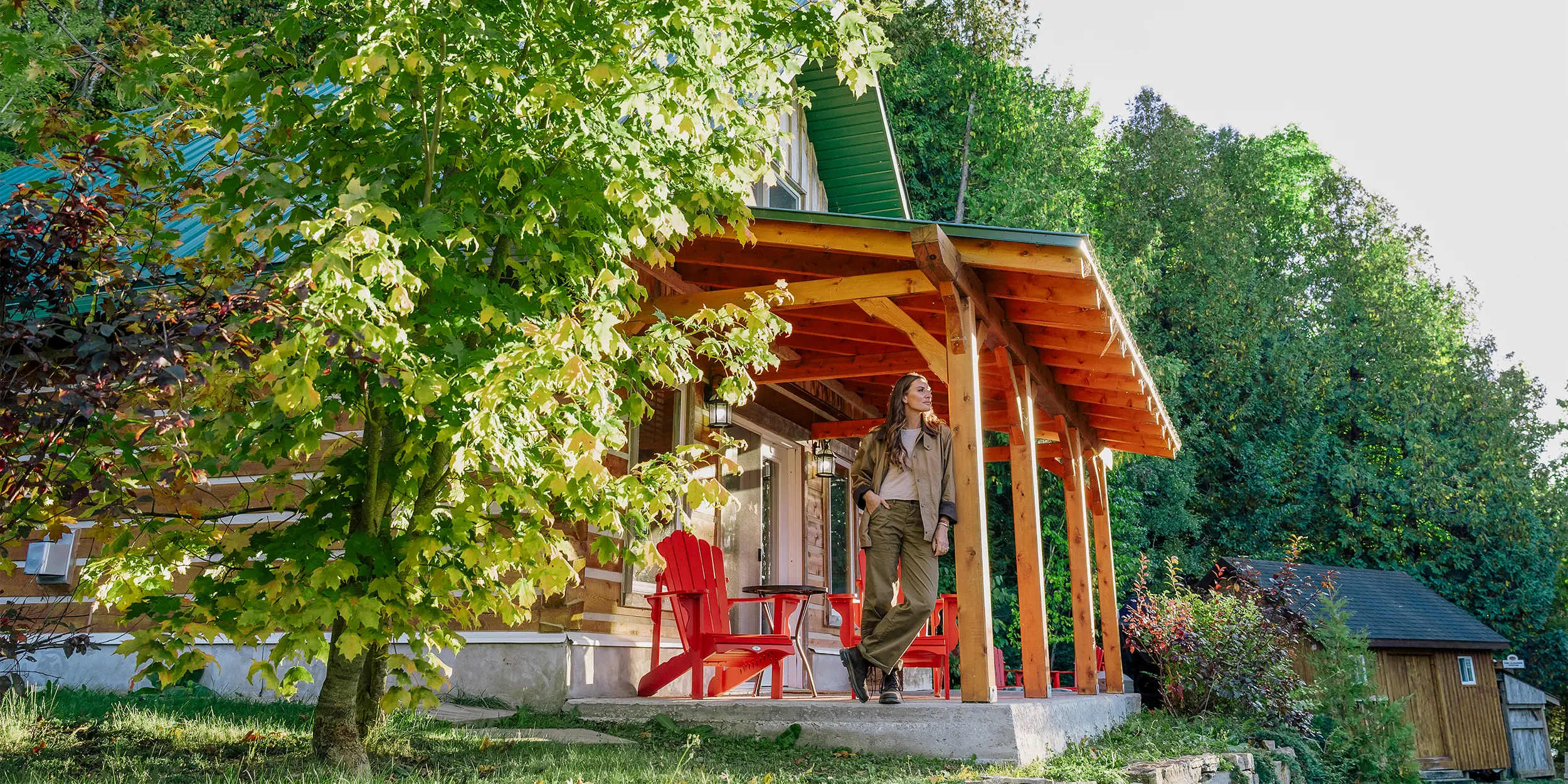 Personne debout sur le porche d’un chalet douillet entouré d’arbres.