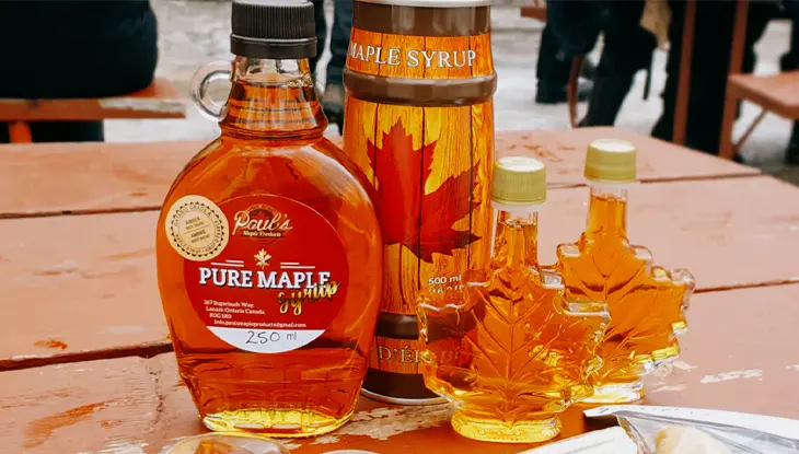 Selection of maple syrup bottles and leaf-shaped containers displayed on a picnic table during a maple festival.