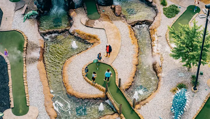 Luftaufnahme eines Minigolfplatzes mit Dinosaurierstatuen, Wasserspielen und Spielern auf dem Platz bei Dinosaur Adventure Golf, Niagara Falls.