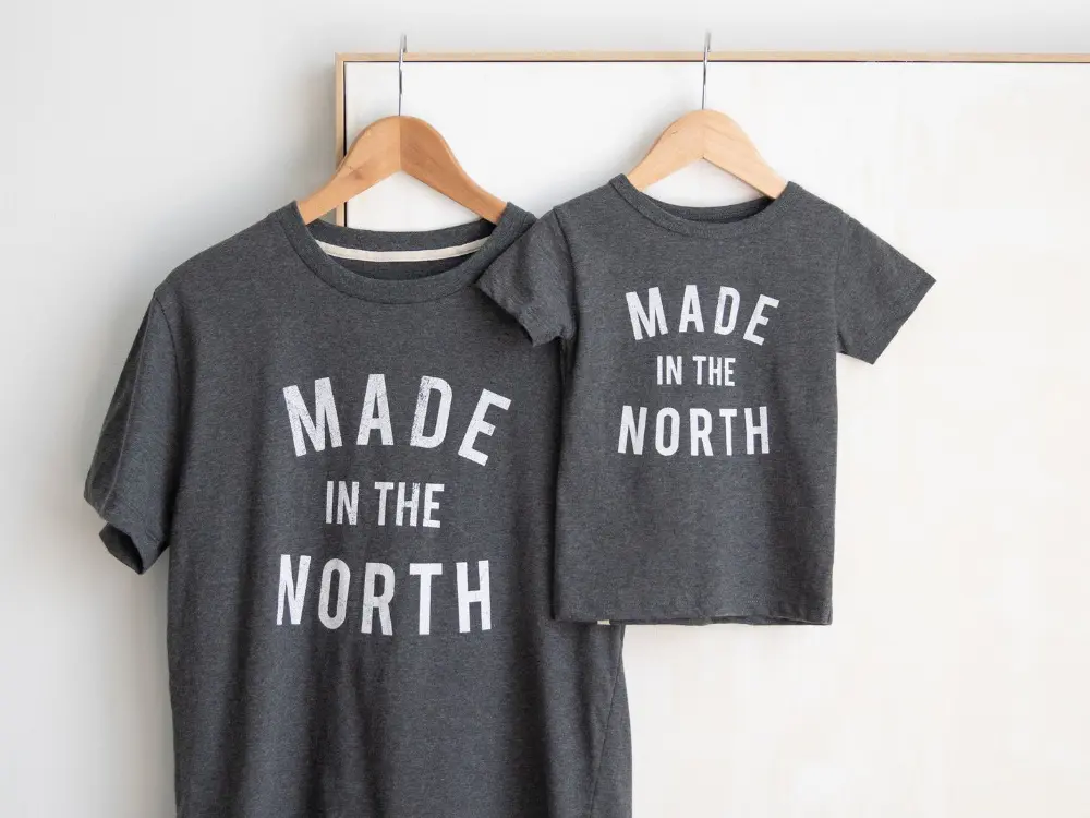 Two t-shirts are displayed in baby and adult sizes, with "Made in the North" written in white text on grey fabric.
