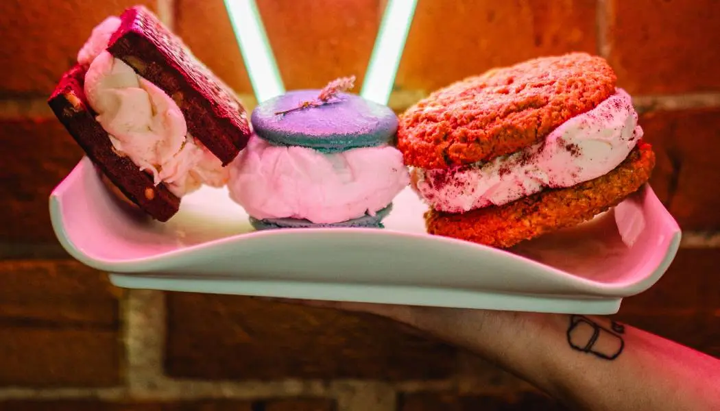 Une personne présente un grand plat à dessert contenant trois généreux sandwichs glacés.