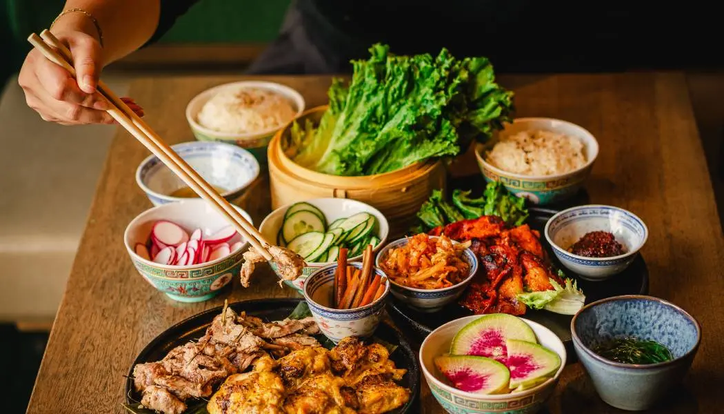 한 손님이 나무 테이블 위에 놓인 여러 가지 색깔의 접시에서 젓가락으로 음식을 집어 먹고 있다.