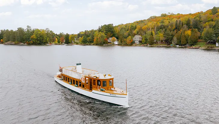 Bateau classique en bois naviguant sur un lac à Muskoka, avec les couleurs d’automne le long des rives.