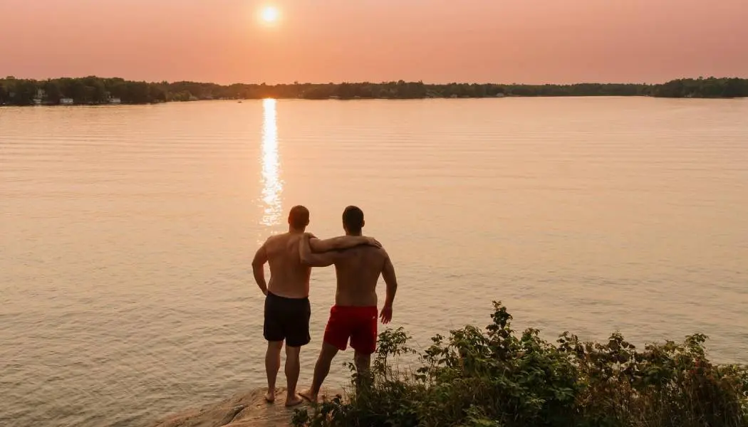 Deux hommes s'enlacent face au coucher du soleil sur un lac.