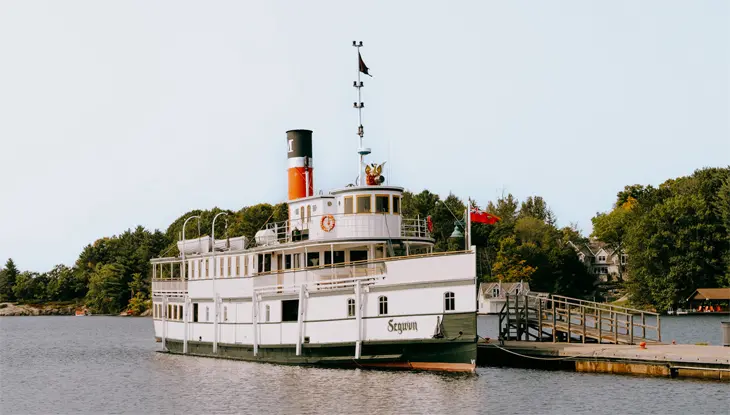A large, stately green and white passenger steamship is docked in Gravenhurst.