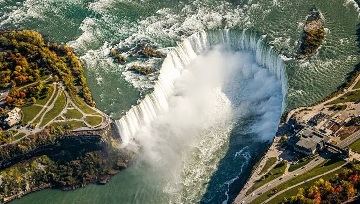 Aerial view of the magnificent Niagara Falls with fall foliage appearing in the surrounding forest.