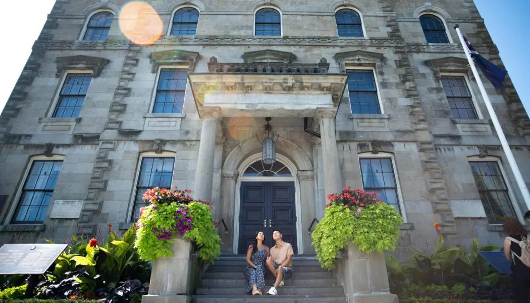 A couple sits on the steps of a historic, stone building in downtown Niagara-on-the-Lake.