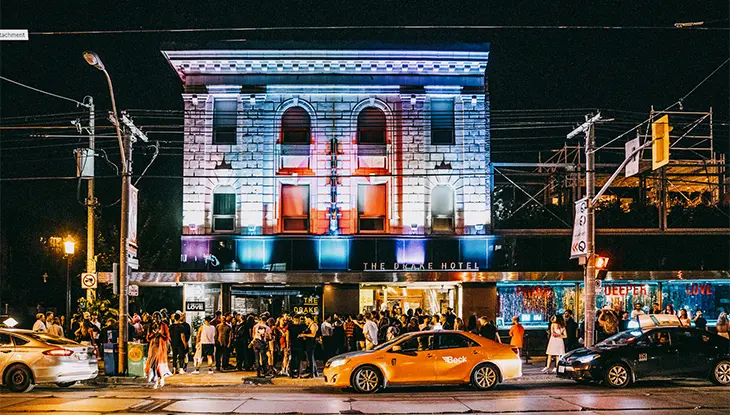 Bâtiment en brique illuminé par des lumières colorées la nuit le long d’une rue animée de la ville.