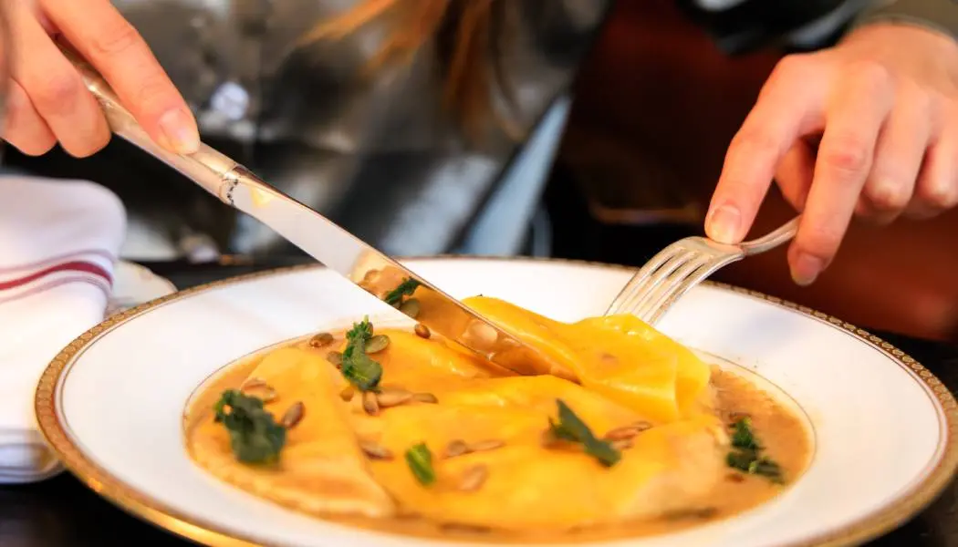Gros plan sur une personne dégustant une assiette de raviolis frais avec une fourchette et une cuillère dans un restaurant chic d'Ottawa.