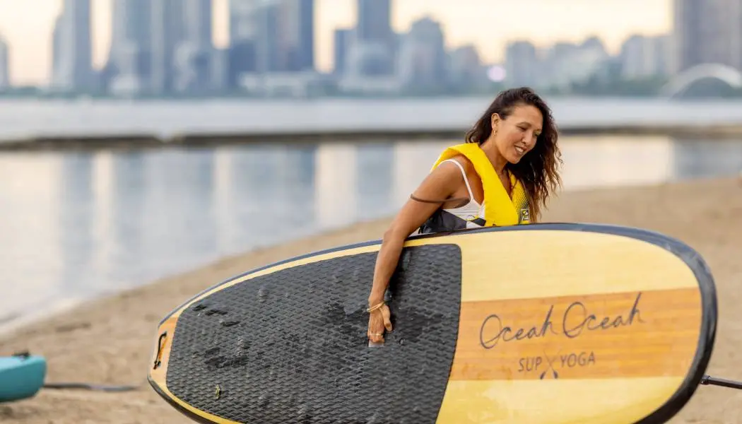 Femme transportant une planche à pagaie en bois sur la plage, dans le secteur riverain de Toronto.